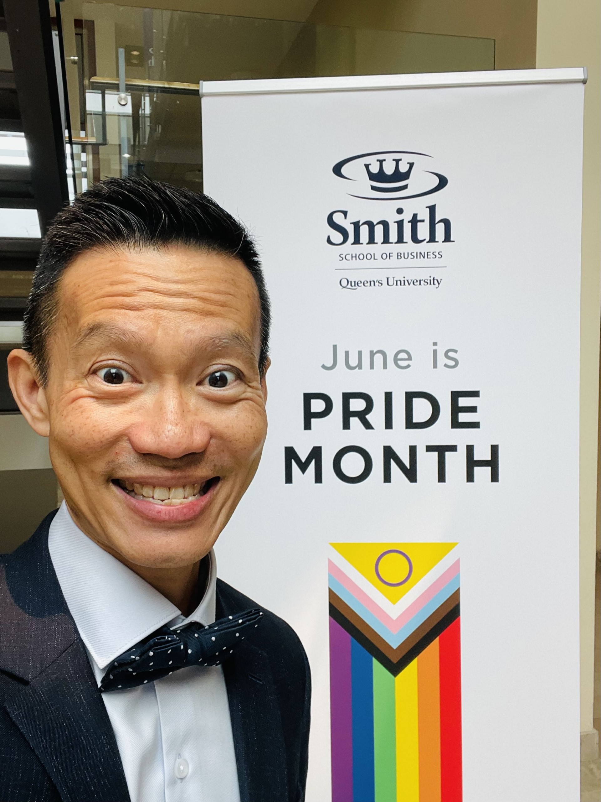 Professor Eddy Ng, Editor-in-Chief of EDI, stands by a sign for Queens University that says 'June is Pride Month'