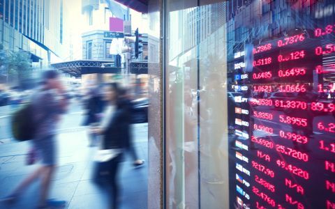 Blurred image of people walking past digital sign featuring exchange rates